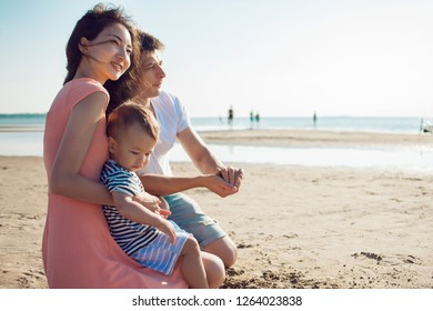 Cheerful Multi Ethnic Family Have A Rest On A Sea Shore. Young Family, Man Woman And Little Son Enjoy Picnic, Summer Outdoor, Good Weather