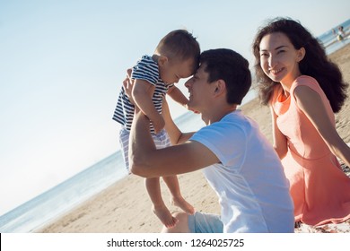 Cheerful Multi Ethnic Family Have A Rest On A Sea Shore. Young Family, Man Woman And Little Son Enjoy Picnic, Summer Outdoor, Good Weather