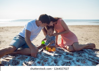 Cheerful Multi Ethnic Family Have A Rest On A Sea Shore. Young Family, Man Woman And Little Son Enjoy Picnic, Summer Outdoor, Good Weather