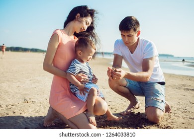 Cheerful Multi Ethnic Family Have A Rest On A Sea Shore. Young Family, Man Woman And Little Son Enjoy Picnic, Summer Outdoor, Good Weather