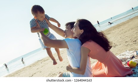 Cheerful Multi Ethnic Family Have A Rest On A Sea Shore. Young Family, Man Woman And Little Son Enjoy Picnic, Summer Outdoor, Good Weather