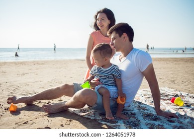 Cheerful Multi Ethnic Family Have A Rest On A Sea Shore. Young Family, Man Woman And Little Son Enjoy Picnic, Summer Outdoor, Good Weather