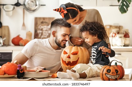 Cheerful multi ethnic family parents with son smiling  while creating jack o lantern from pumpkin during Halloween celebration in kitchen at home - Shutterstock ID 1833746497