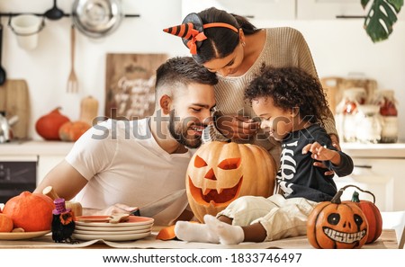 Cheerful multi ethnic family parents with son smiling  while creating jack o lantern from pumpkin during Halloween celebration in kitchen at home Foto stock © 