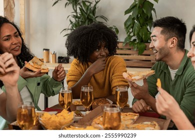 Cheerful multi ethnic friends enjoying a meal together at home, eating pizza and nachos, drinking beer, chatting and laughing, having a great time - Powered by Shutterstock