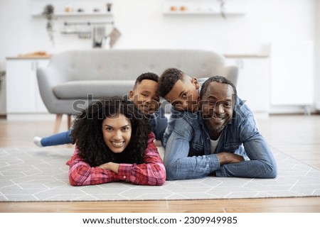 Cheerful multicultural mom and dad carrying happy children on their backs while lying on floor indoors. Active parents enjoying playful form of exercise while boys getting creative entertainment.