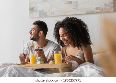 cheerful multiethnic couple eating breakfast in bed - Powered by Shutterstock