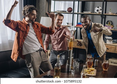 cheerful multiethnic men friends having fun and looking at tower from bottles and glasses while partying indoors