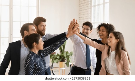 Cheerful multiethnic team of young professionals giving group high five, enjoying teamwork spirit, celebrating job success, achievement, win, successful cooperation, shouting for joy