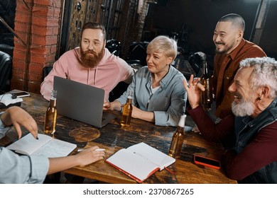 cheerful multiethnic workmates listening to colleague near laptop and beer bottles in pub after work - Powered by Shutterstock