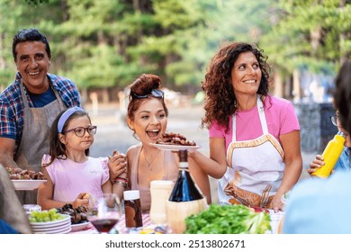 Cheerful multigenerational family enjoying outdoor barbecue in forest setting. Parents, children, and friends sharing meal at picnic table - Family bonding, summer activities, and outdoor dining. - Powered by Shutterstock