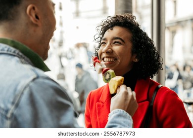 Cheerful multiracial couple is enjoying a valentine's day treat, sharing a fruit skewer filled with pineapple, kiwi, and strawberries, creating a romantic and playful atmosphere - Powered by Shutterstock