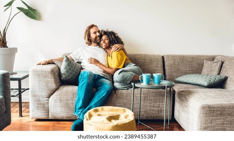 Cheerful multiracial couple sitting on sofa in the living room - Happy family moving in new home - Real estate and stylish furniture concept - Powered by Shutterstock