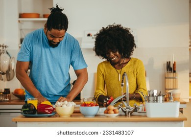 A cheerful multiracial couple is standing in a kitchen and doing chores at home. A woman is washing dishes in a kitchen sink while her husband is preparing and cooking a vegan dinner at home. - Powered by Shutterstock