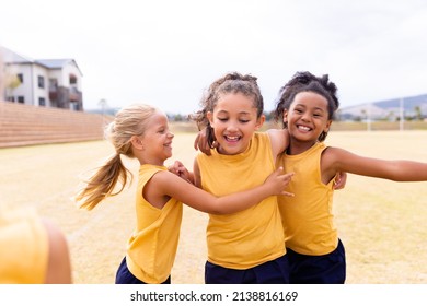 Cheerful Multiracial Elementary School Girls In Sports Uniform On Ground During Soccer Practice. Unaltered, Childhood, Education, Sports Training And Sports Activity Concept.