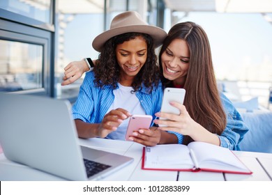 Cheerful multiracial female best friend share multimedia files on smartphones spending free time together,smiling hipster girls synchronizing telephone sending photos and video sitting at cafe