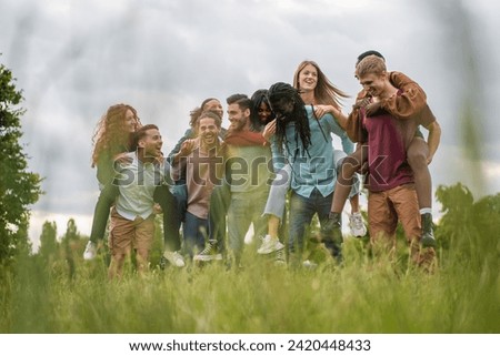 Cheerful multiracial friends engage in piggyback fun, laughing in a natural outdoor setting, epitomizing group unity.