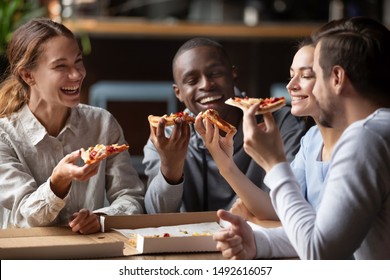Cheerful multiracial happy best friends couples laugh at funny joke eating pizza in cafe together, happy multicultural young mates having fun sharing food at party meeting in pizzeria sit at table