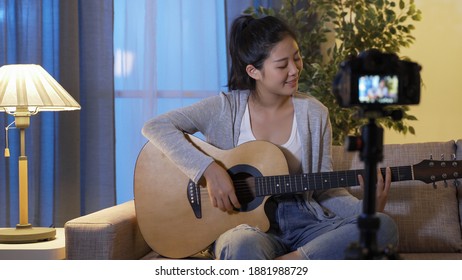 Cheerful Music Influencer Waving Hands To Greet Her Fans In Front Of Digital Camera And Starting To Play The Guitar On Sofa While Shooting Live Performance Video At Home