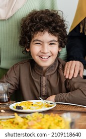 cheerful muslim arabian boy looking at camera near pilaf during family dinner