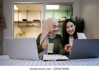 Cheerful Muslim girlfriends in had near face smiling while planning further work together and using laptop and learning at home.  - Powered by Shutterstock