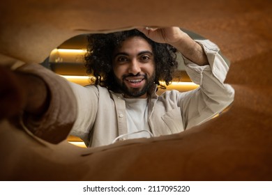 Cheerful Muslim man with kinky hair opens paper bag to take out products delivered from grocery store in kitchen close view from inside