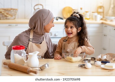 Cheerful Muslim Woman In Hijab Baking In Kitchen With Her Little Daughter, Islamic Mom And Her Small Child Having Fun While Preparring Pastry For Cookies Together, Kneading Dough And Smiling - Shutterstock ID 1923705698