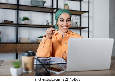 cheerful muslim woman pointing at laptop during online lesson at home - Shutterstock ID 2124454673