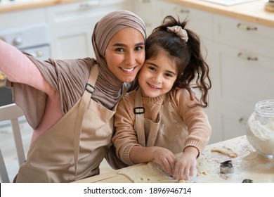 Cheerful Muslim Woman Taking Selfie With Her Little Daughter In Kitchen. Cute Happy Child And Her Islamic Mom Wearing Aprons, Posing At Camera Together While Baking At Home, Closeup - Powered by Shutterstock