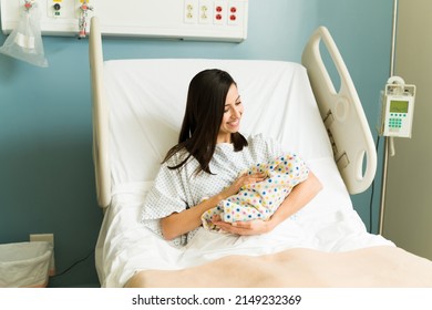 Cheerful new mother carrying and smiling to her newborn baby while resting on the hospital bed after giving birth - Powered by Shutterstock