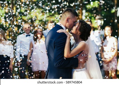 Cheerful newlyweds kiss on porch under the rain of white confetti