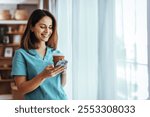 A cheerful nurse in scrubs holds a coffee cup and smiles at her phone. She appears relaxed and content during a break, capturing a moment of happiness and communication.