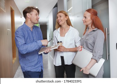 Cheerful Office Workers Talking In The Corridor While Having Coffee Break