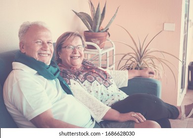 Cheerful old aged senior happy couple sit down on the sofa at home together smiling and staying fine looking at the camera for a portrait family - relax at home concept