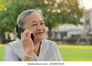 Cheerful old Asian woman excited on receiving some good news over smartphone at park. Copy space. - Powered by Shutterstock