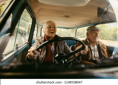 Cheerful old couple driving in a car. Enjoying road trip. Senior woman driving car with woman enjoying the ride and laughing.