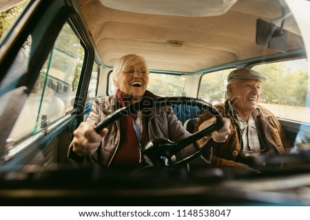 Cheerful old couple driving in a car. Enjoying road trip. Senior woman driving car with woman enjoying the ride and laughing.