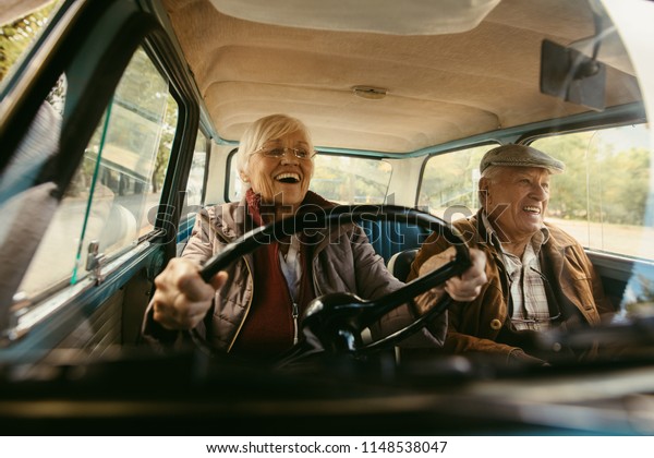 Cheerful old couple driving in a car. Enjoying\
road trip. Senior woman driving car with woman enjoying the ride\
and laughing.