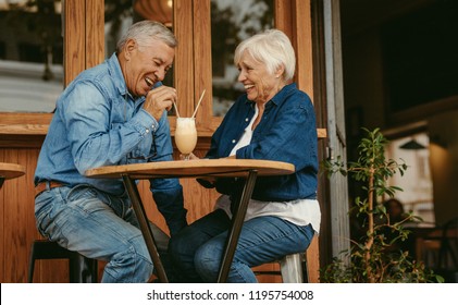 Cheerful old couple sitting at cafe having a coffee. Senior man and woman sitting at restaurant table talking with cold coffee on table.