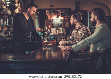 Cheerful old friends drinking draft beer at bar counter in pub.