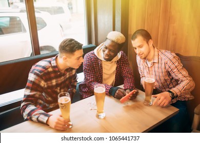 Cheerful old friends having fun with smartphone and drinking draft beer in pub.