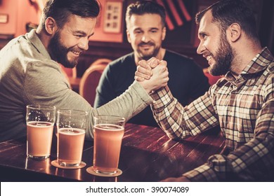 Cheerful old friends having fun arm wrestling each other in pub.