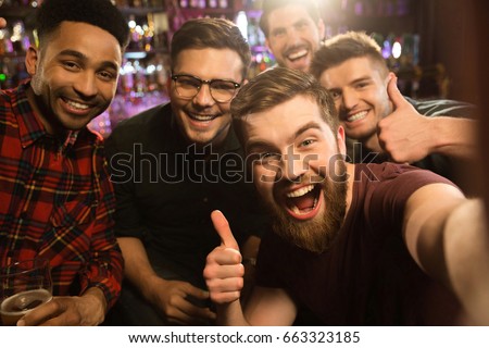 Cheerful old friends having fun by taking selfie and drinking draft beer in pub