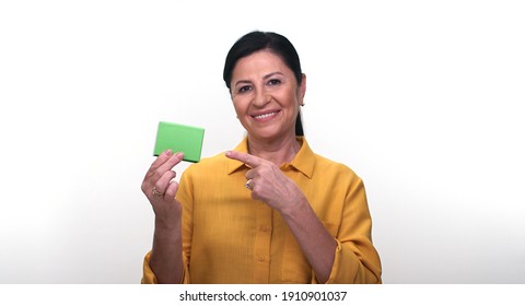 Cheerful Old Lady Holding Small Green Box In Hand And Pointing With Her Finger, Isolated On White Background. Creative People Can Put The Product They Want In The Woman's Hand.