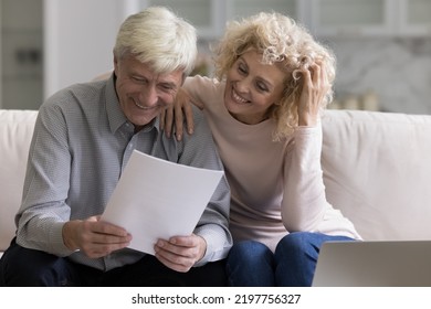 Cheerful Old Mature Married Couple Reading Paper Document At Laptop On Home Couch, Reviewing Notice, Checking Insurance, Mortgage Agreement, Getting Investment Income. Retirement, Paperwork