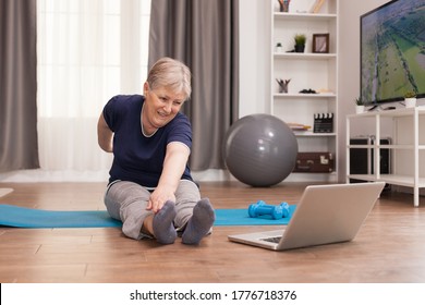 Cheerful Old Woman Doing Sports Watching Online Lessons. Old Person Pensioner Online Internet Exercise Training At Home Sport Activity With Dumbbell, Resistance Band, Swiss Ball At Elderly Retirement