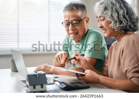 Cheerful older Asian couple working on a laptop planning their retirement finances looking at investment options. They are considering property and savings for their future home.