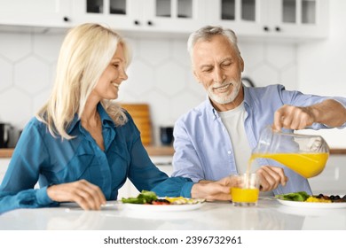 Cheerful Older Spouses Enjoying Healthy Breakfast Together In Kitchen, Happy Senior Couple Enjoying Delicious Food At Home, Caring Husband Pouring Orange Juice From Jug, Closeup Shot - Powered by Shutterstock