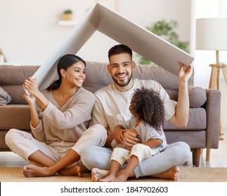 Fröhliche Eltern mit Kindern, die während der Umsiedlung im gemütlichen Wohnzimmer auf dem Boden lächeln und das Dach über Kopf halten
