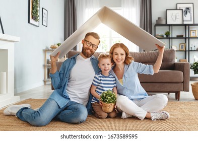 Fröhliche Eltern mit Kindern, die während der Umsiedlung im gemütlichen Wohnzimmer auf dem Boden sitzen und das Dach über Kopf lächeln und halten